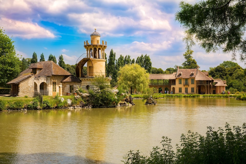 Ein historischer Gebäudekomplex mit einem Turm, einem Teich und umliegenden Bäumen.