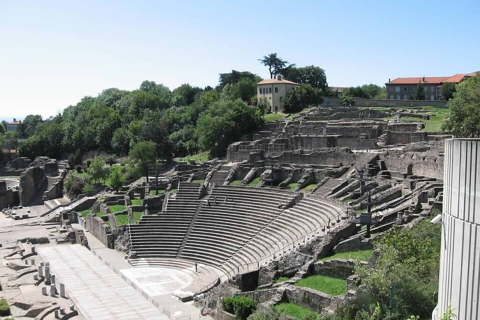 An ancient amphitheater surrounded by lush greenery and modern buildings.