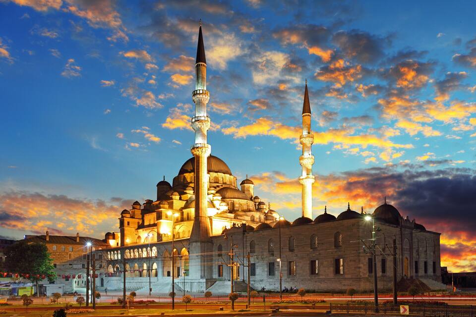 A historic mosque with multiple domes and minarets, illuminated at dusk.