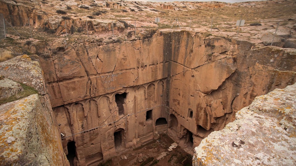A large, ancient rock formation with multiple caves and a fenced-off area.