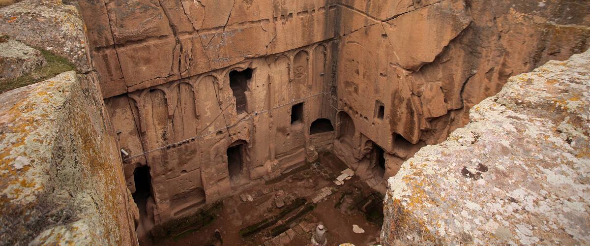 A large, ancient rock formation with multiple caves and a fenced-off area.