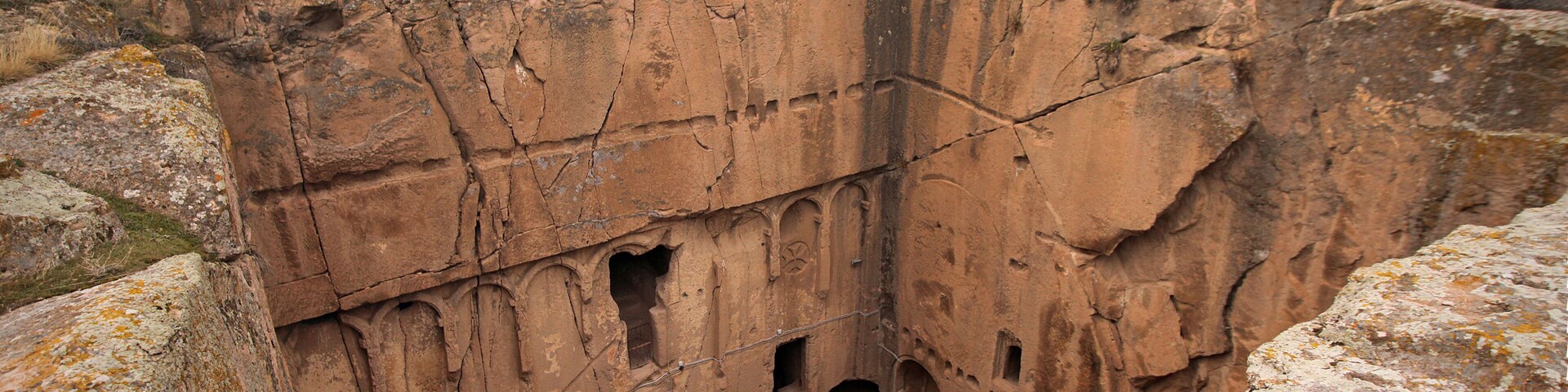 A large, ancient rock formation with multiple caves and a fenced-off area.