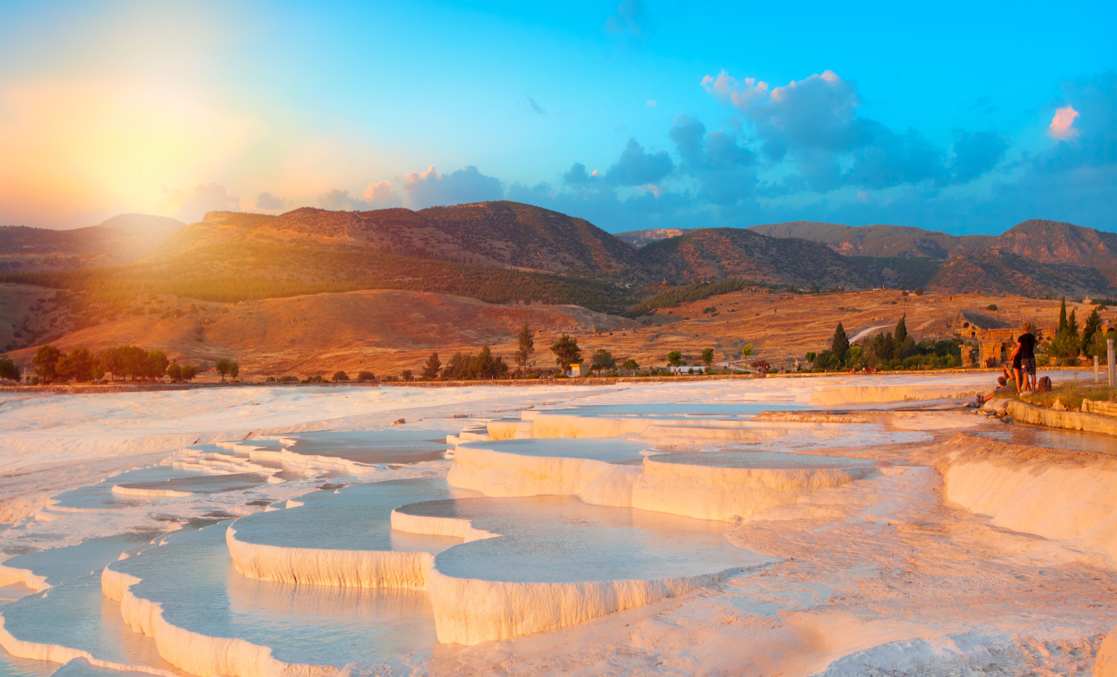 Terraced mineral pools, a mountainous backdrop, and a clear sky.