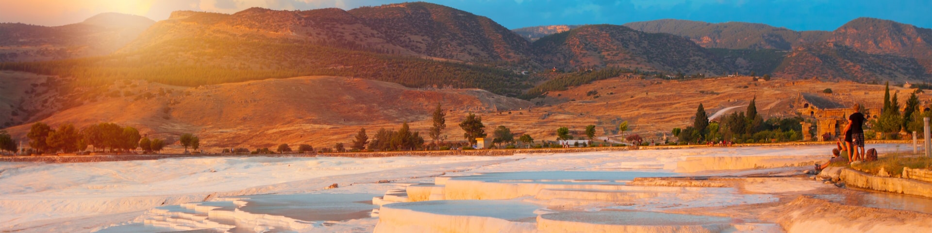 Terraced mineral pools, a mountainous backdrop, and a clear sky.