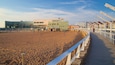 Une plage de sable avec un terrain de volleyball, un bâtiment moderne et une clôture blanche le long de la promenade.