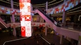 Un centre commercial à plusieurs niveaux, doté d’escalators, d’un grand écran vertical illuminé et de divers magasins, dont Zara.