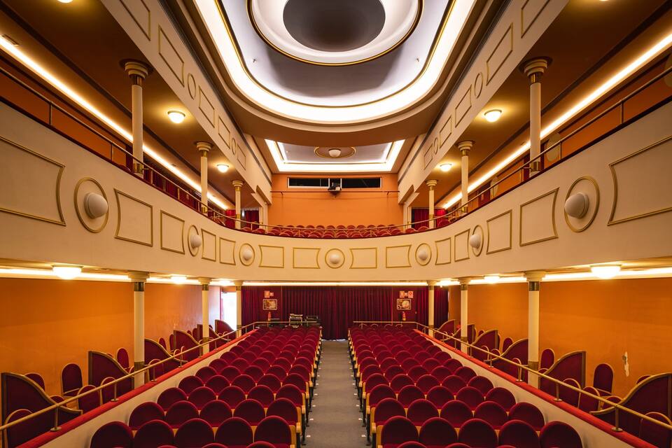 Un théâtre avec des sièges rouges, une allée centrale et un balcon.