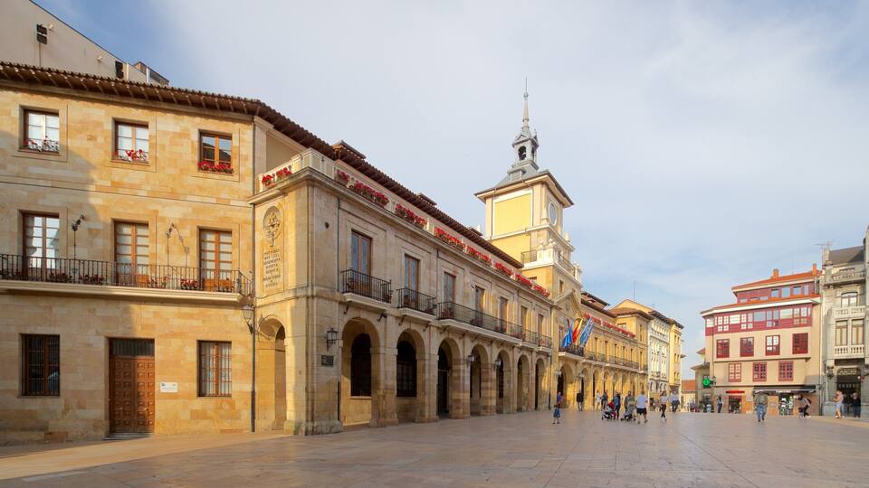 A historic plaza with a prominent building featuring a clock tower and arched walkways.