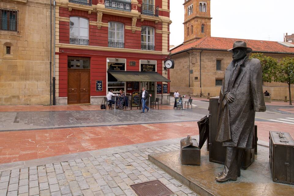 A statue of a man in a suit and hat, a building with a red facade, and a clock tower in the background.