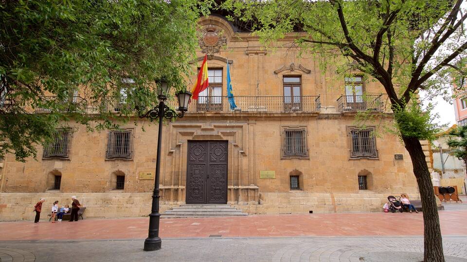 A historic building with a large ornate door, flags, and a tree in the foreground.