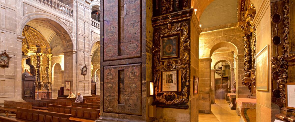 An ornate church interior with wooden pews, stone columns, and religious artwork.