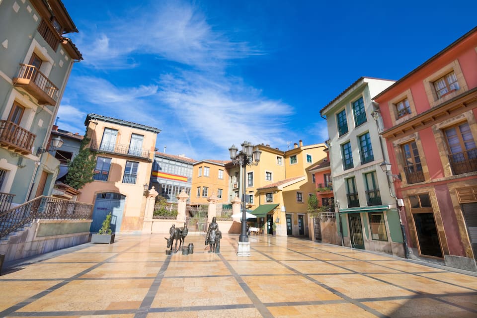A plaza with a tiled floor, colorful buildings, and a statue of people.