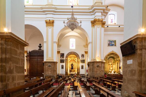Interior de igreja com bancos de madeira, altar central e lustre.