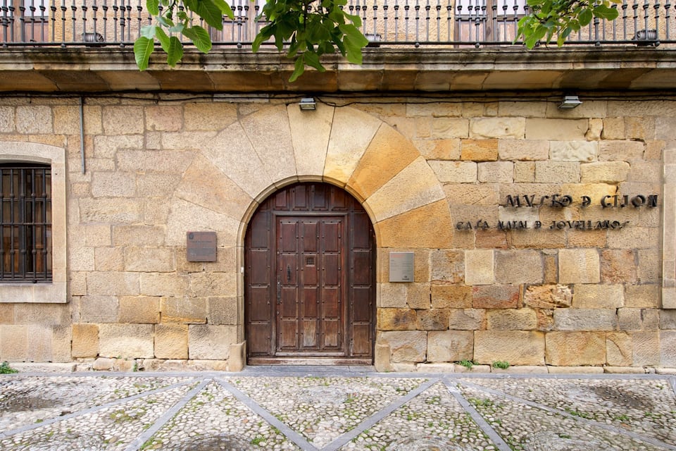 A stone building with a large wooden door and a plaque reading "Museo de la Casa de Pilatos".