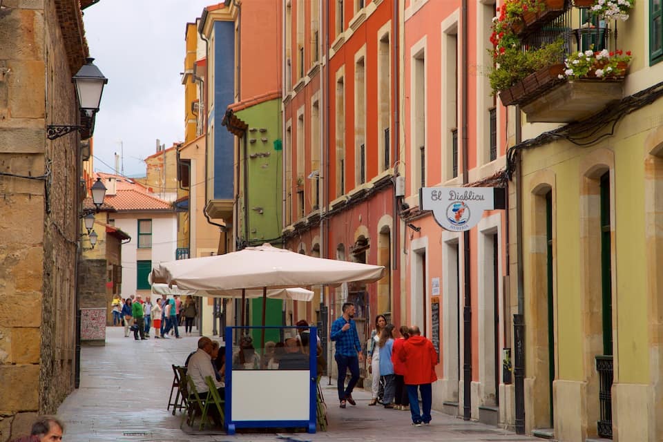 A narrow street with colorful buildings, a street vendor cart, and pedestrians.