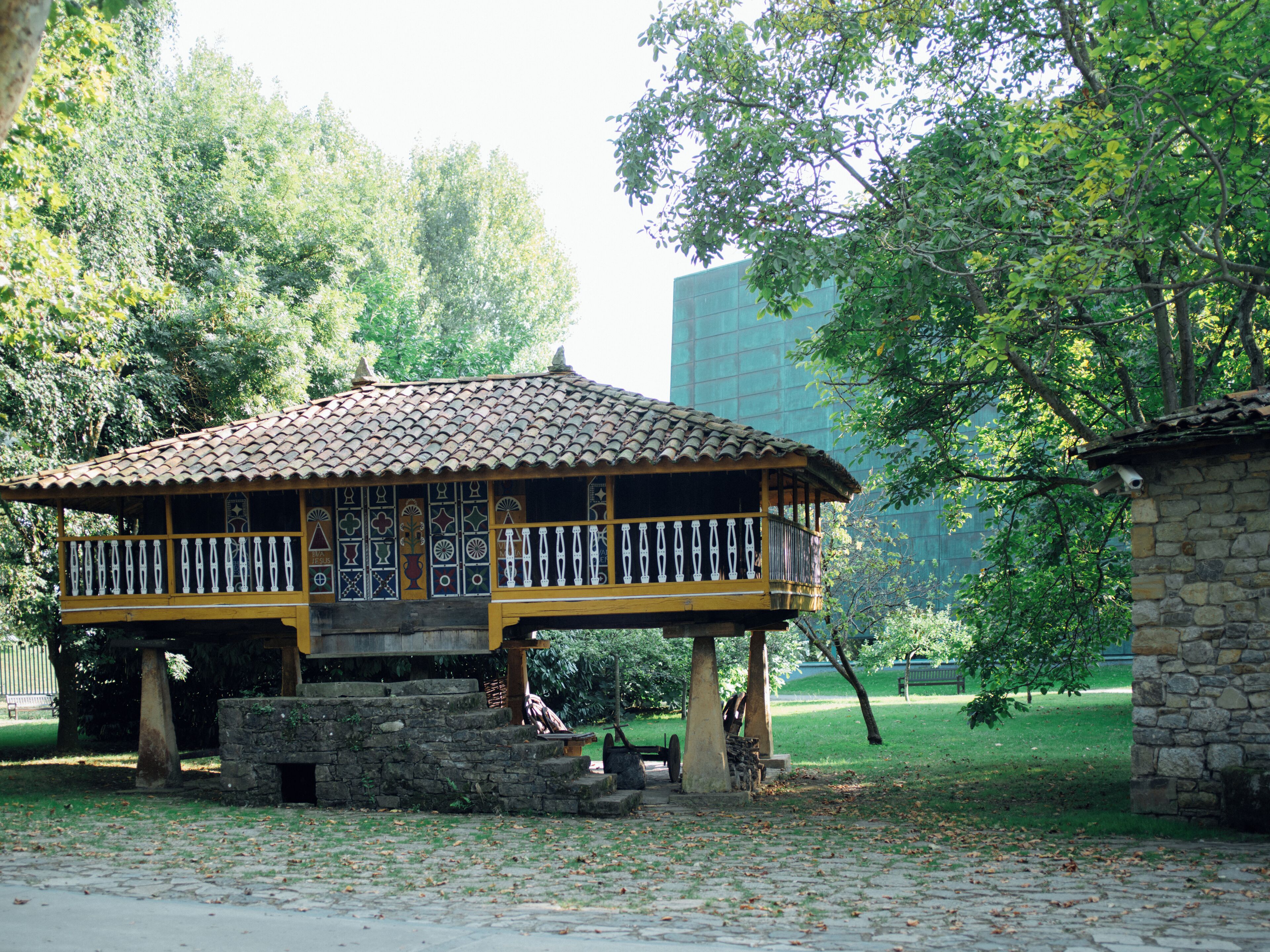 Un pavillon traditionnel en bois, doté d’un toit en tuiles, entouré d’une végétation luxuriante et d’un mur de pierre.