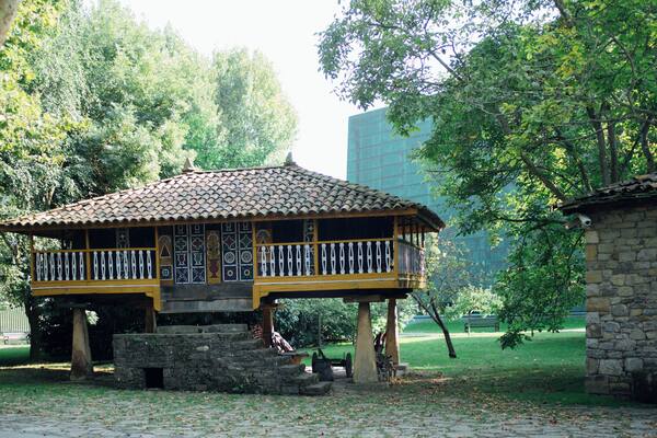 Un pavillon traditionnel en bois, doté d’un toit en tuiles, entouré d’une végétation luxuriante et d’un mur de pierre.