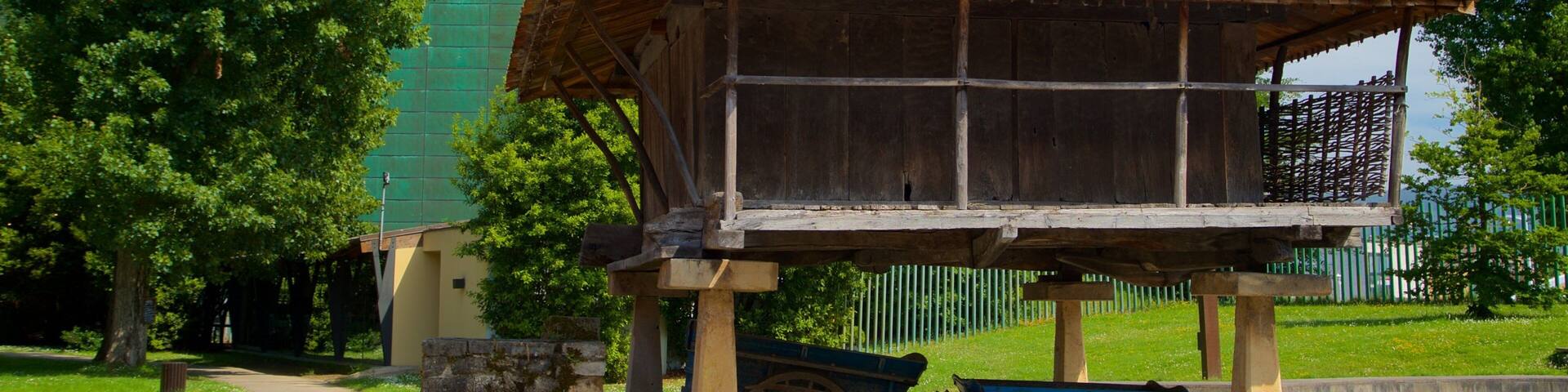 A rustic wooden structure with a tiled roof, a blue wheelbarrow, and a stone pillar.