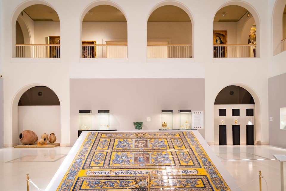 A museum interior with a large tiled floor, arched ceilings, and glass display cases.