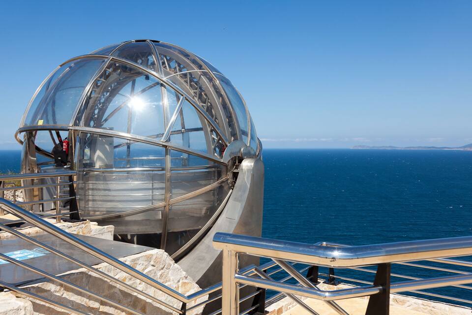 A glass-enclosed observation wheel with metal railings and a clear view of the sea.