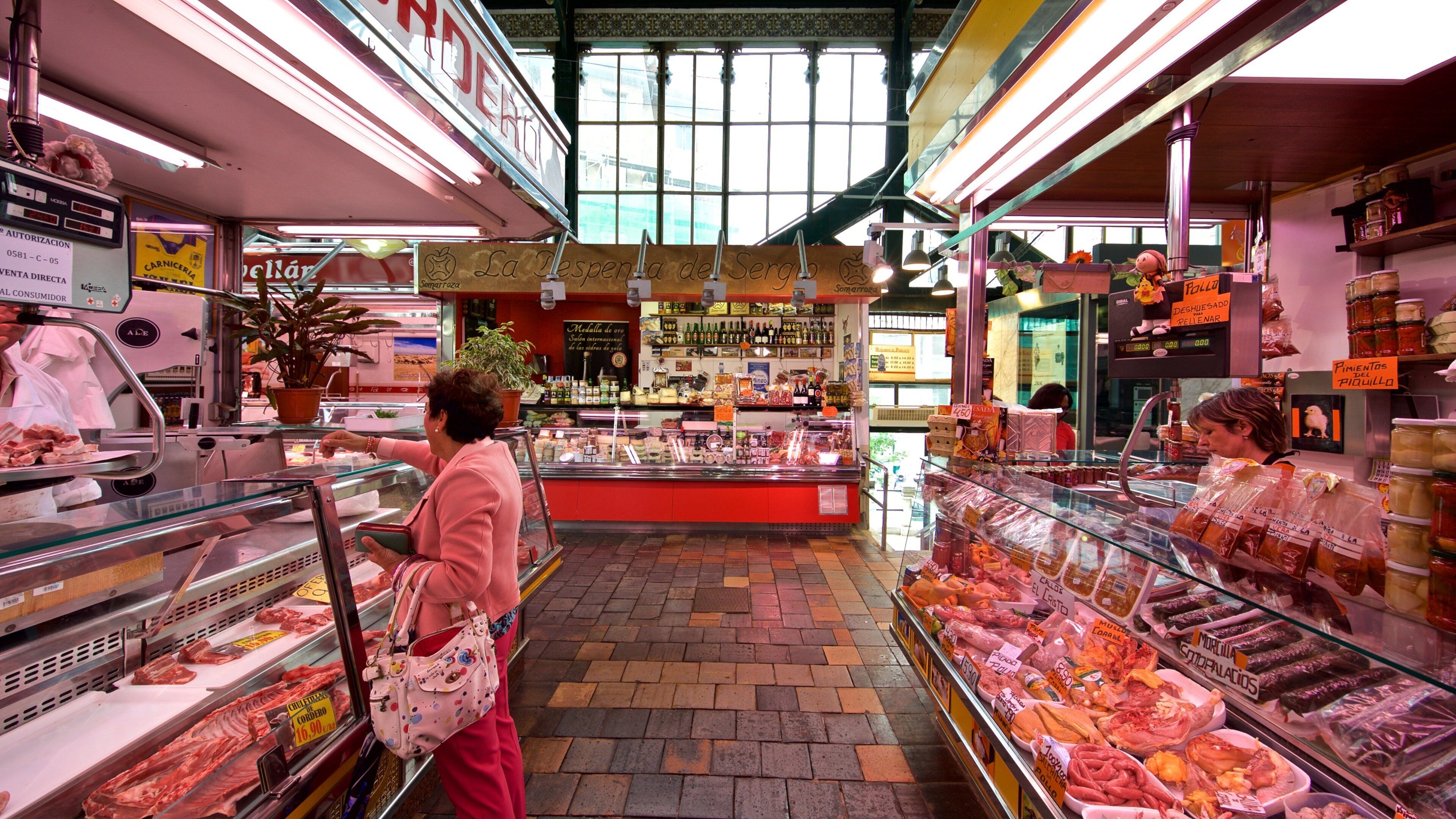 A butcher shop with glass display cases filled with various meats and a woman shopping.