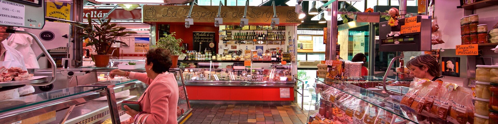 Una carnicería con vitrinas de vidrio repletas de diferentes tipos de carne y una mujer de compras.
