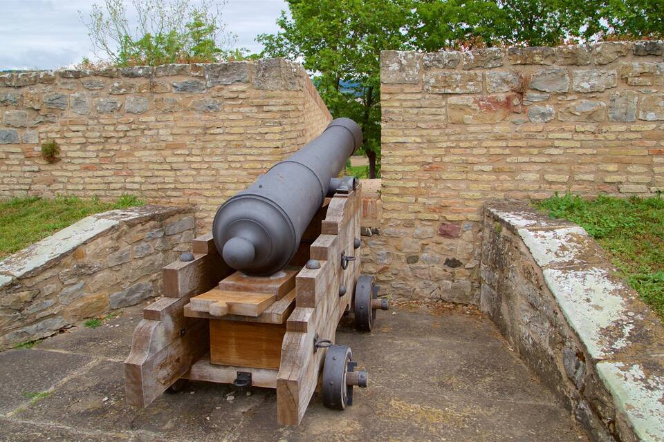 A large cannon mounted on a wooden carriage, positioned between two stone walls.