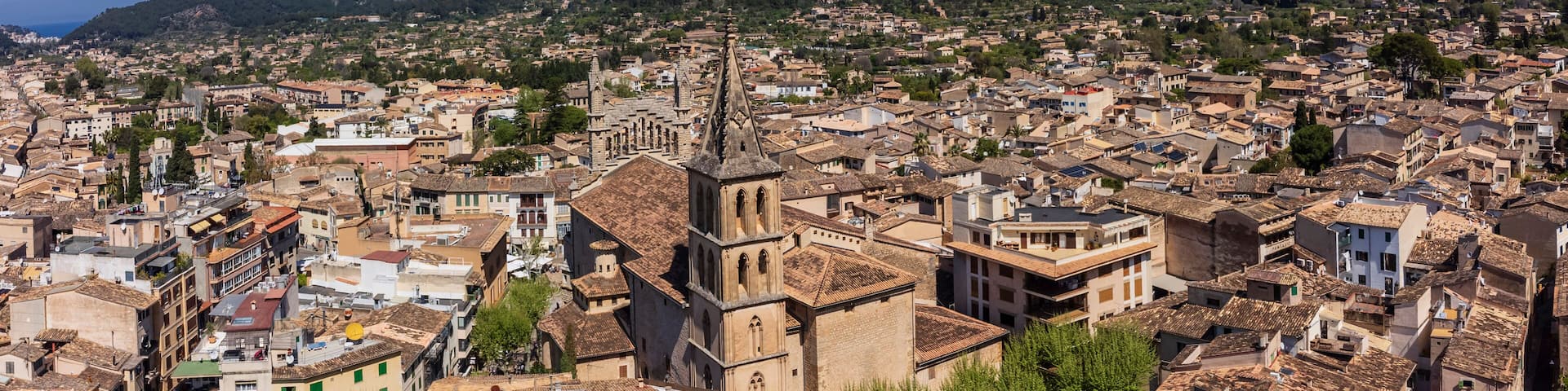 A densely packed urban area with historic architecture, including a prominent church with a bell tower, set against a backdrop of mountains.