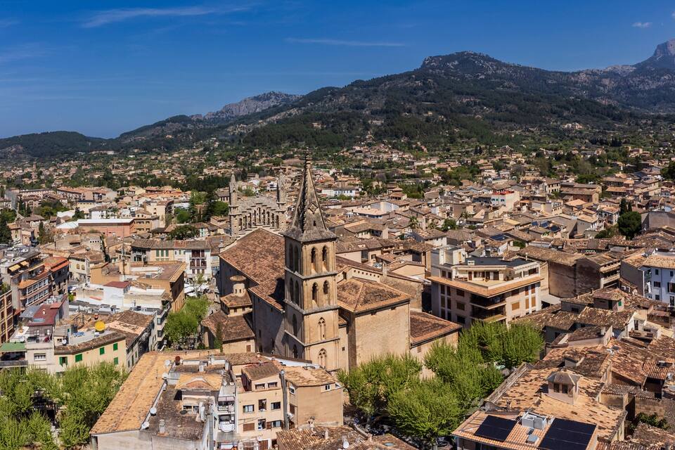 A densely packed urban area with historic architecture, including a prominent church with a bell tower, set against a backdrop of mountains.