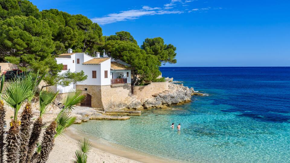 A coastal scene with a white building, clear turquoise waters, and lush greenery.