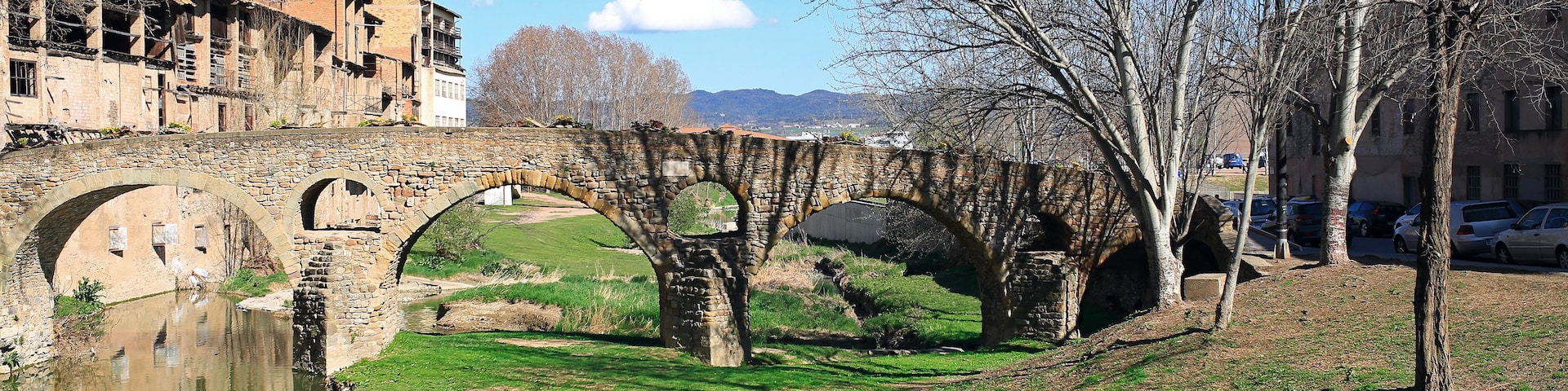 Un pont de pierre enjambe une rivière paisible, entouré de prairies et d’arbres.