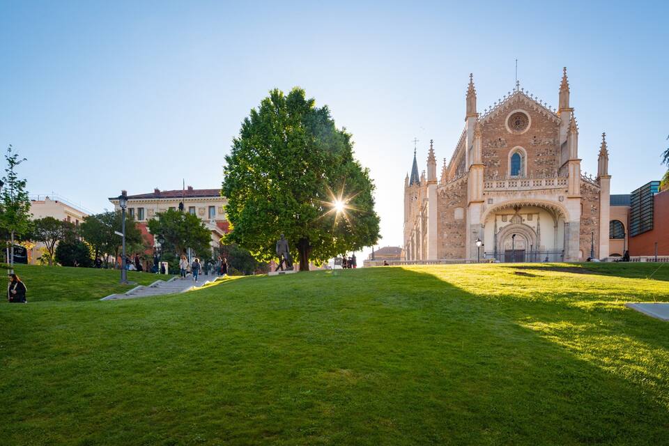 Eine große Kathedrale mit einem markanten Rosasfenster und zwei Türmen, umgeben von einer gepflegten Rasenfläche, auf der einige Personen spazieren gehen.