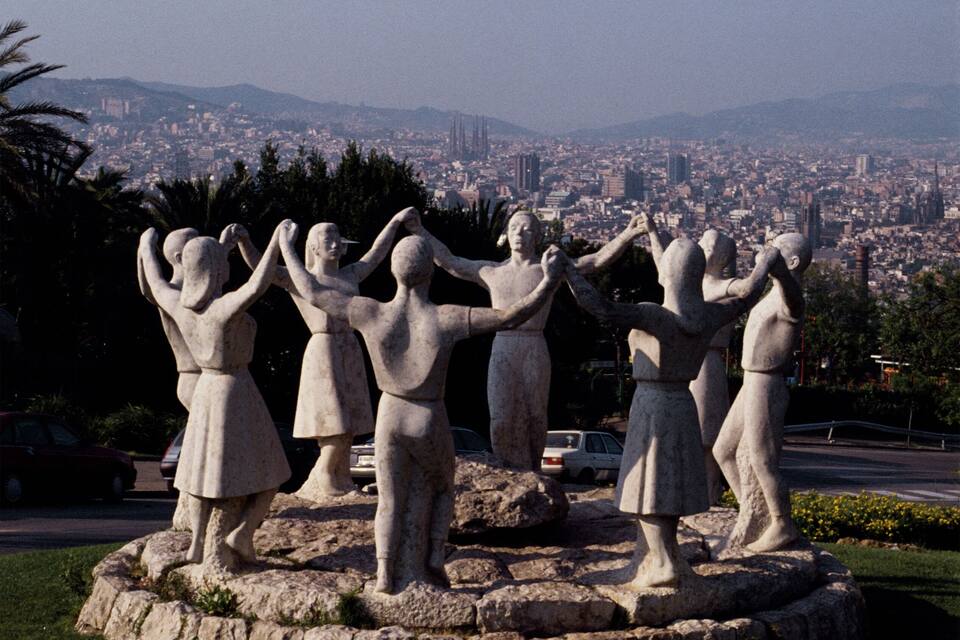 A sculpture of children in a park with a cityscape in the background.