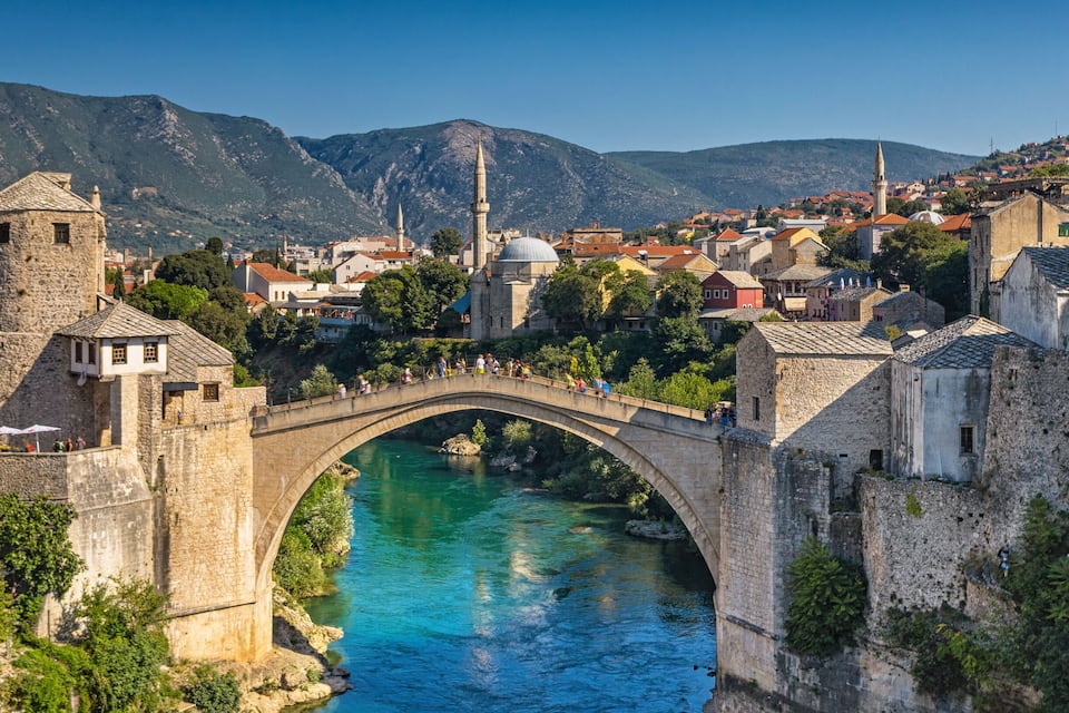 A stone bridge over a river, historic buildings, and a mosque with a minaret.