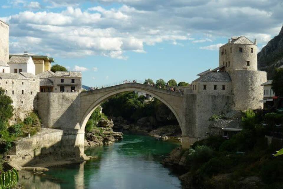 A stone bridge over a river, surrounded by historic buildings and greenery.