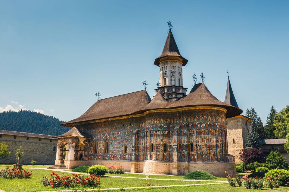 A historic building with a tower, surrounded by a well-maintained garden with red flowers.
