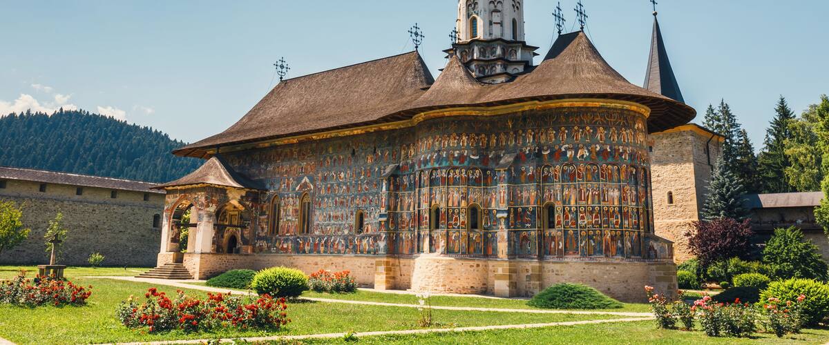 A historic building with a tower, surrounded by a well-maintained garden with red flowers.