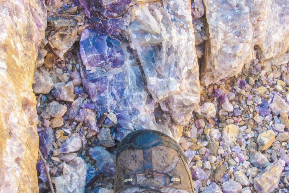 A pair of hiking boots on a rocky terrain with variously colored stones.