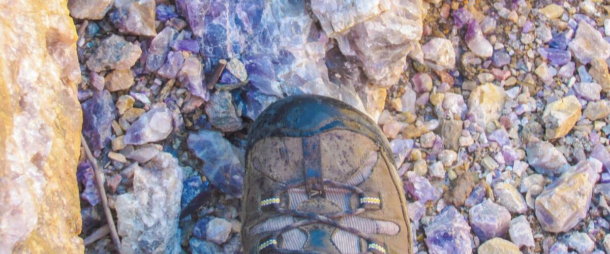 A pair of hiking boots on a rocky terrain with variously colored stones.