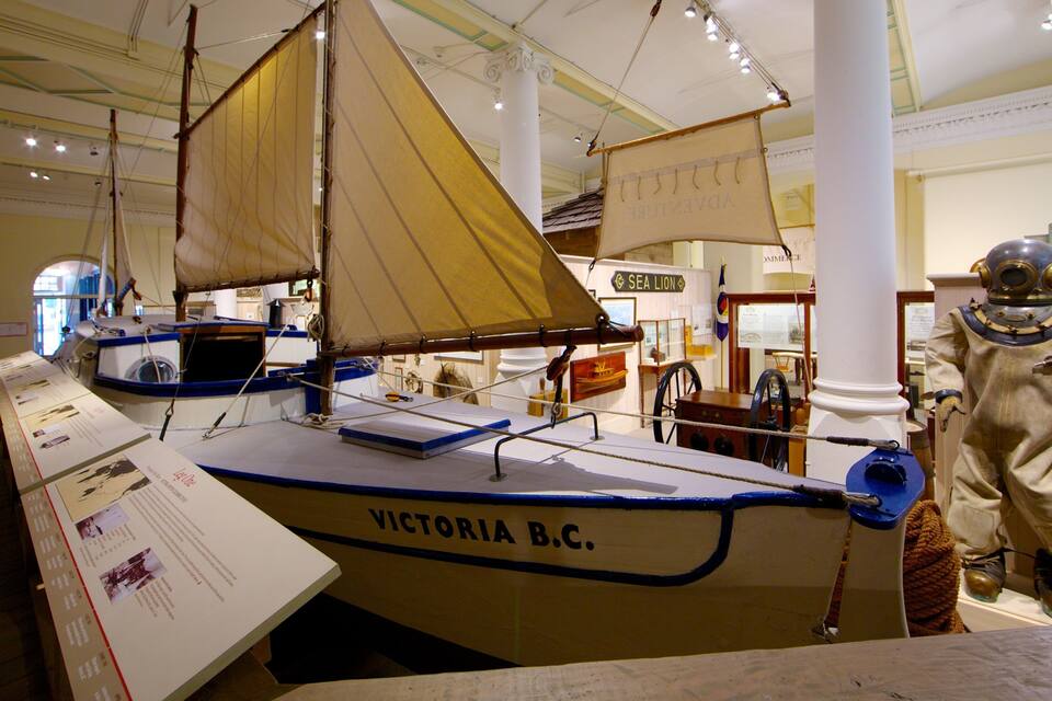 Una maqueta del barco de vela Victoria B.C. exhibida en un museo, con una figura de astronauta cerca.