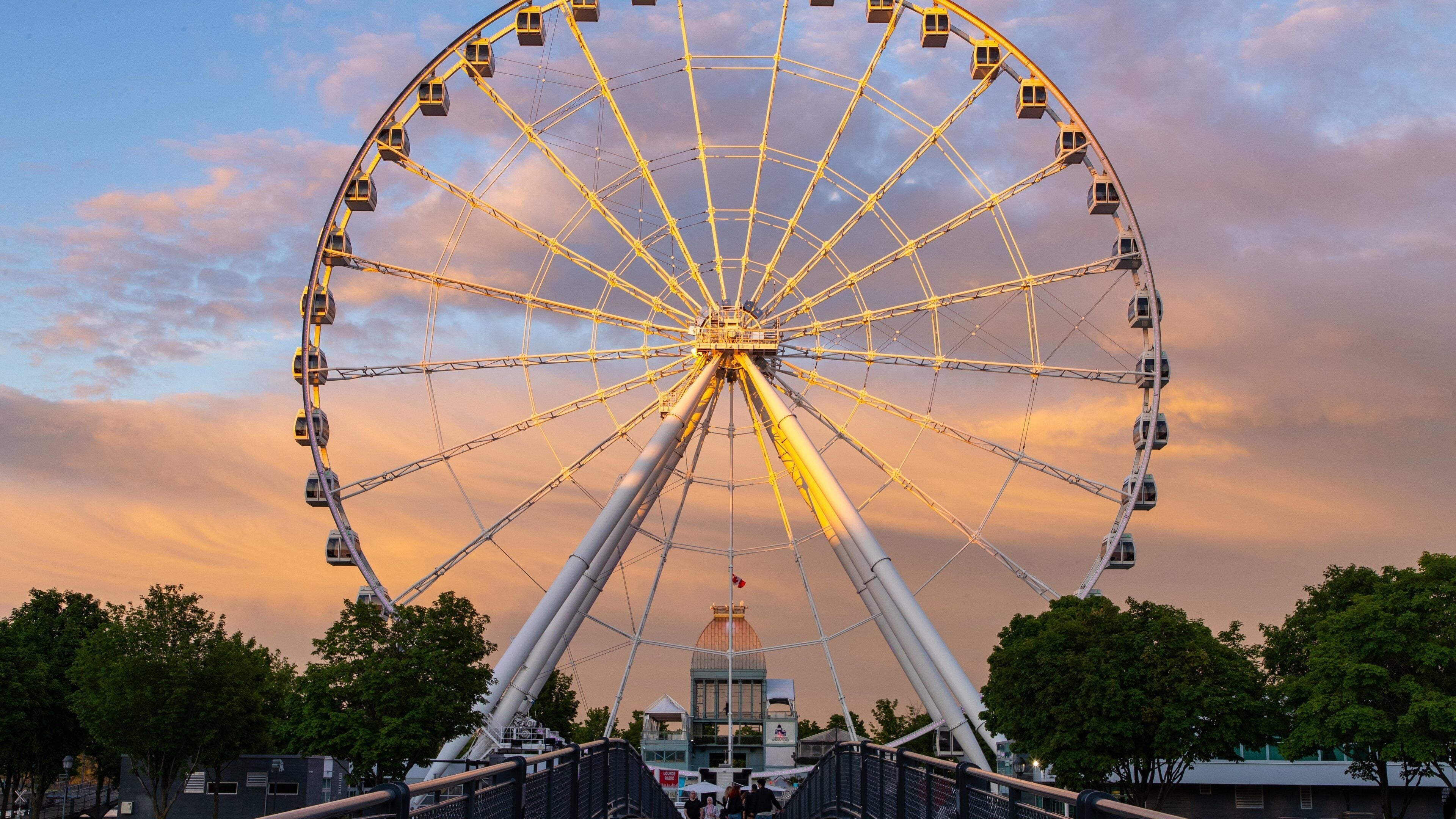Ein großes Riesenrad mit Gondeln, einem zentralen Turm und einem Sonnenuntergangshimmel.
