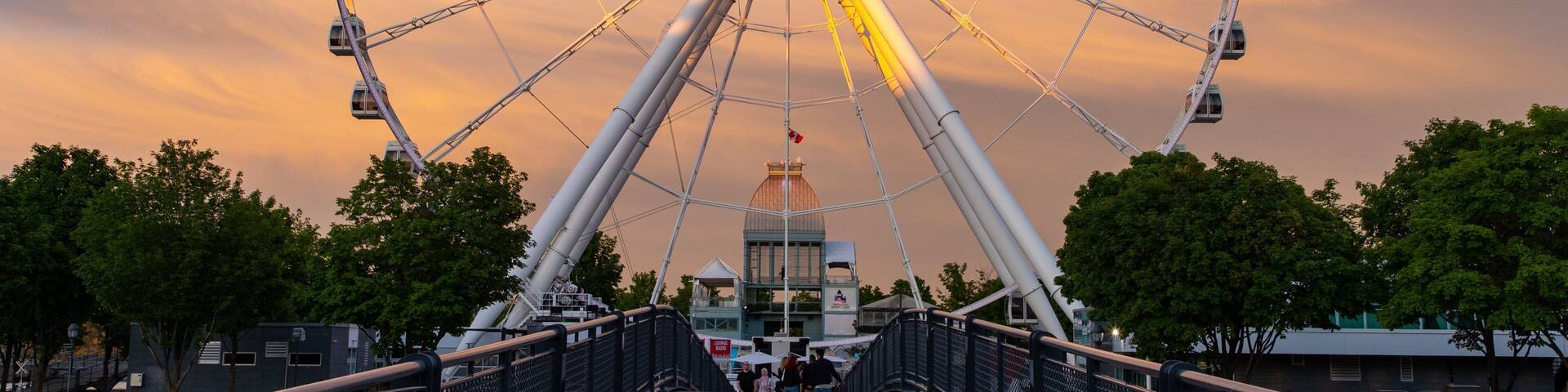 A large Ferris wheel with cabins, a central tower, and a sunset sky.