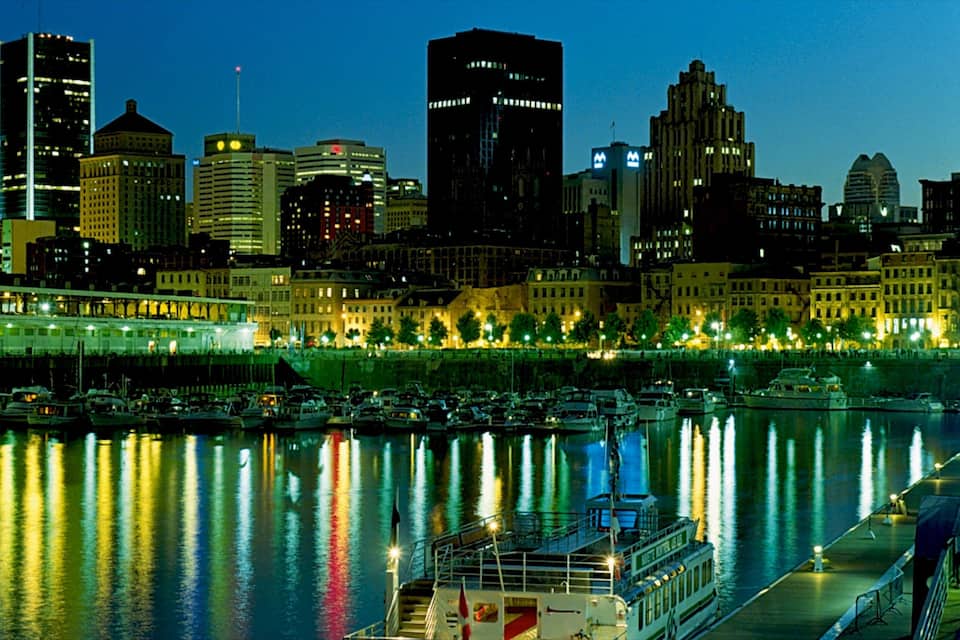 A city skyline at night with illuminated buildings and a marina with boats.