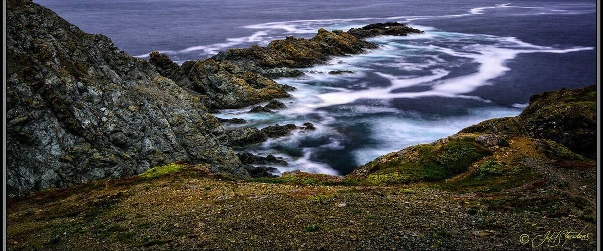 A rugged coastline with rocky outcrops and waves crashing against them.