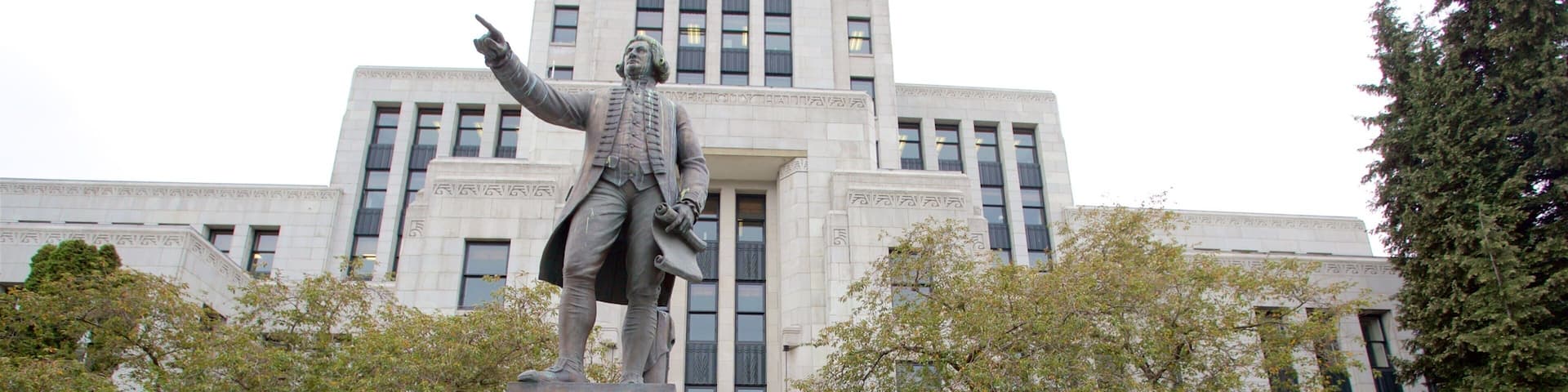 Una estatua del Capitán George Vancouver sobre un pedestal frente a un gran edificio con varias ventanas y una puerta.
