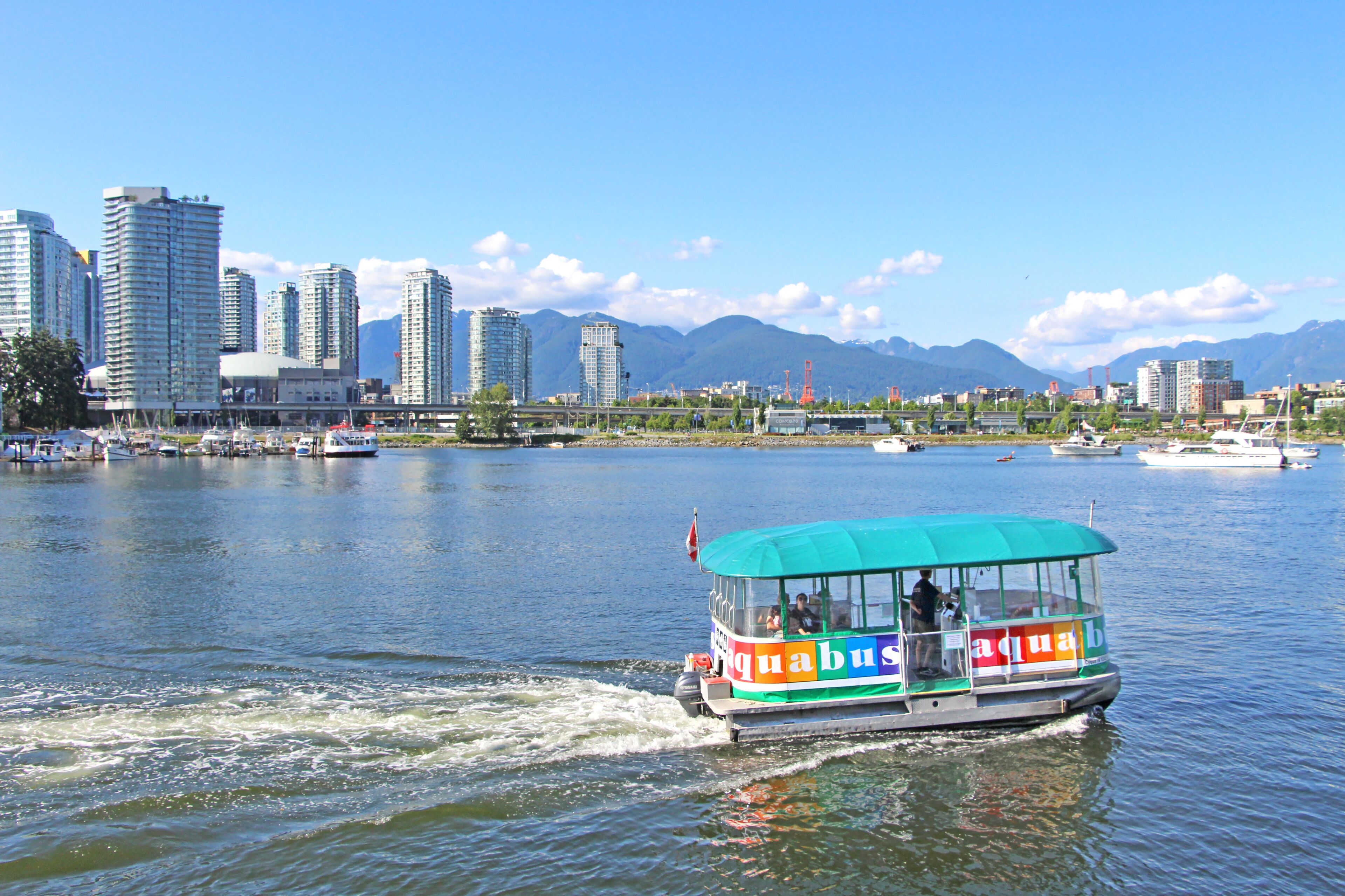 Olympic Village - Aqua Bus in Vancouver, BC. The view on the public transport boat with passengers on. Cityscape - Downtown and mountains in the background.