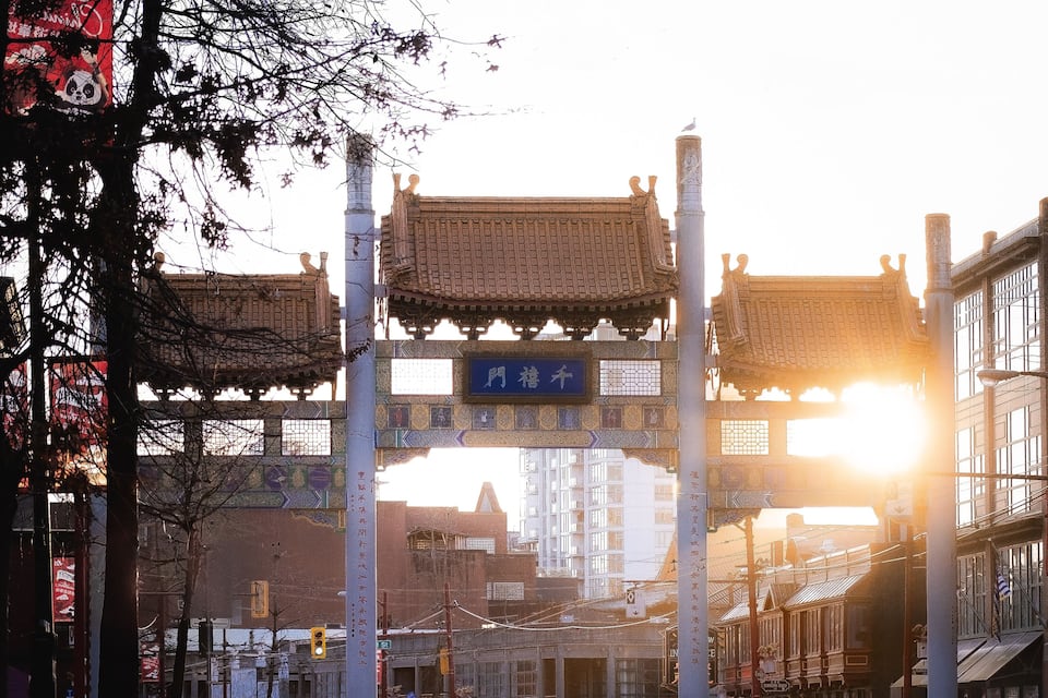 A traditional gate with Chinese characters, a street with cars, and modern buildings in the background.