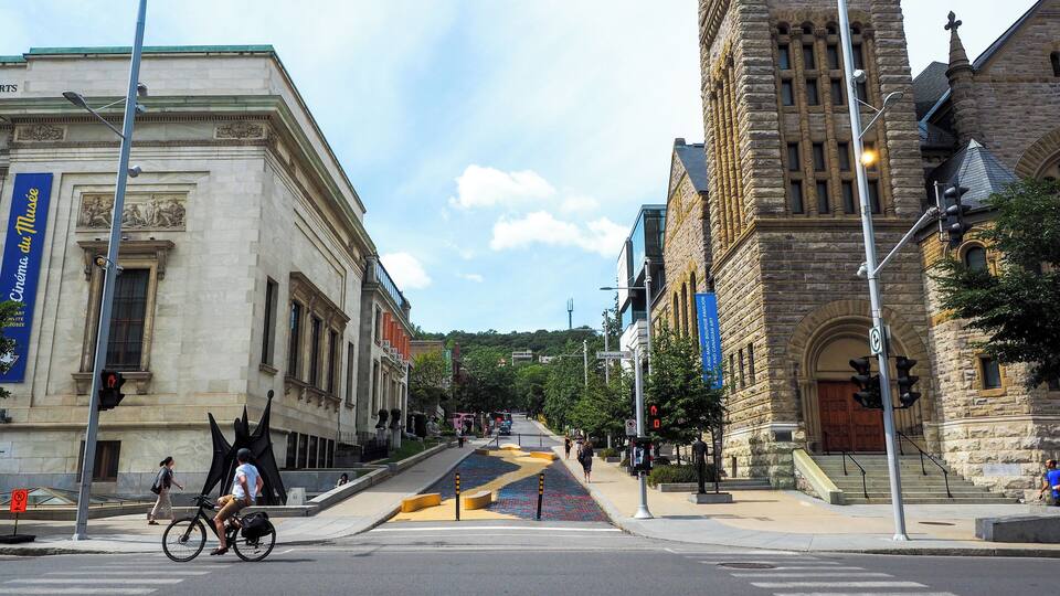 A street with a large stone building, a crosswalk, and a cyclist.