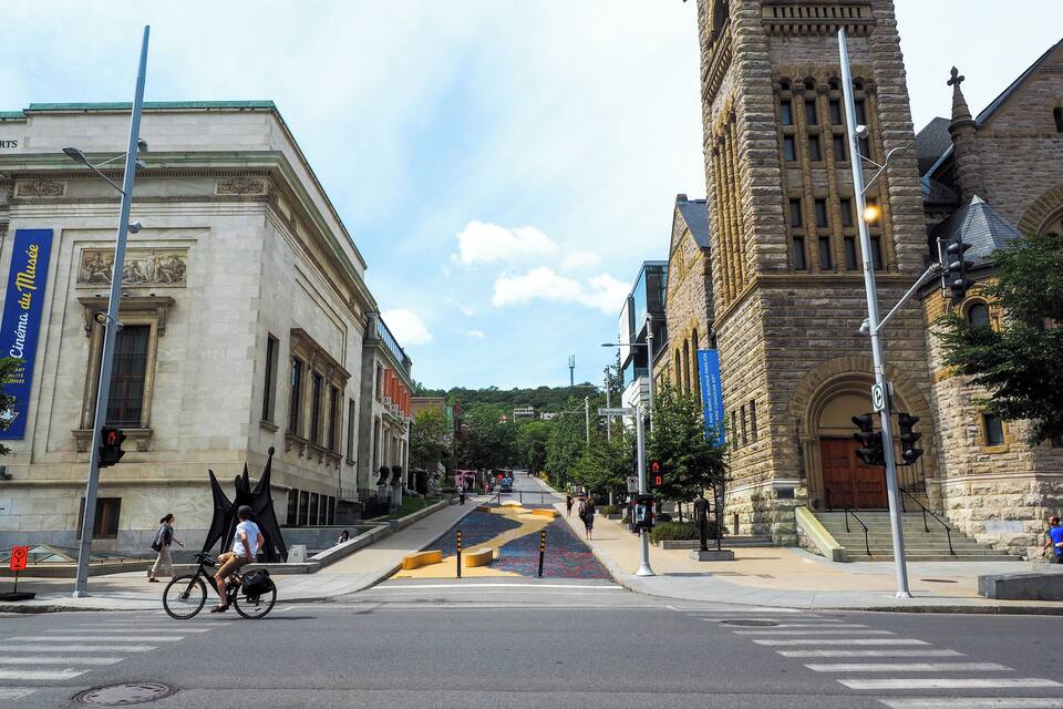 A street with a large stone building, a crosswalk, and a cyclist.