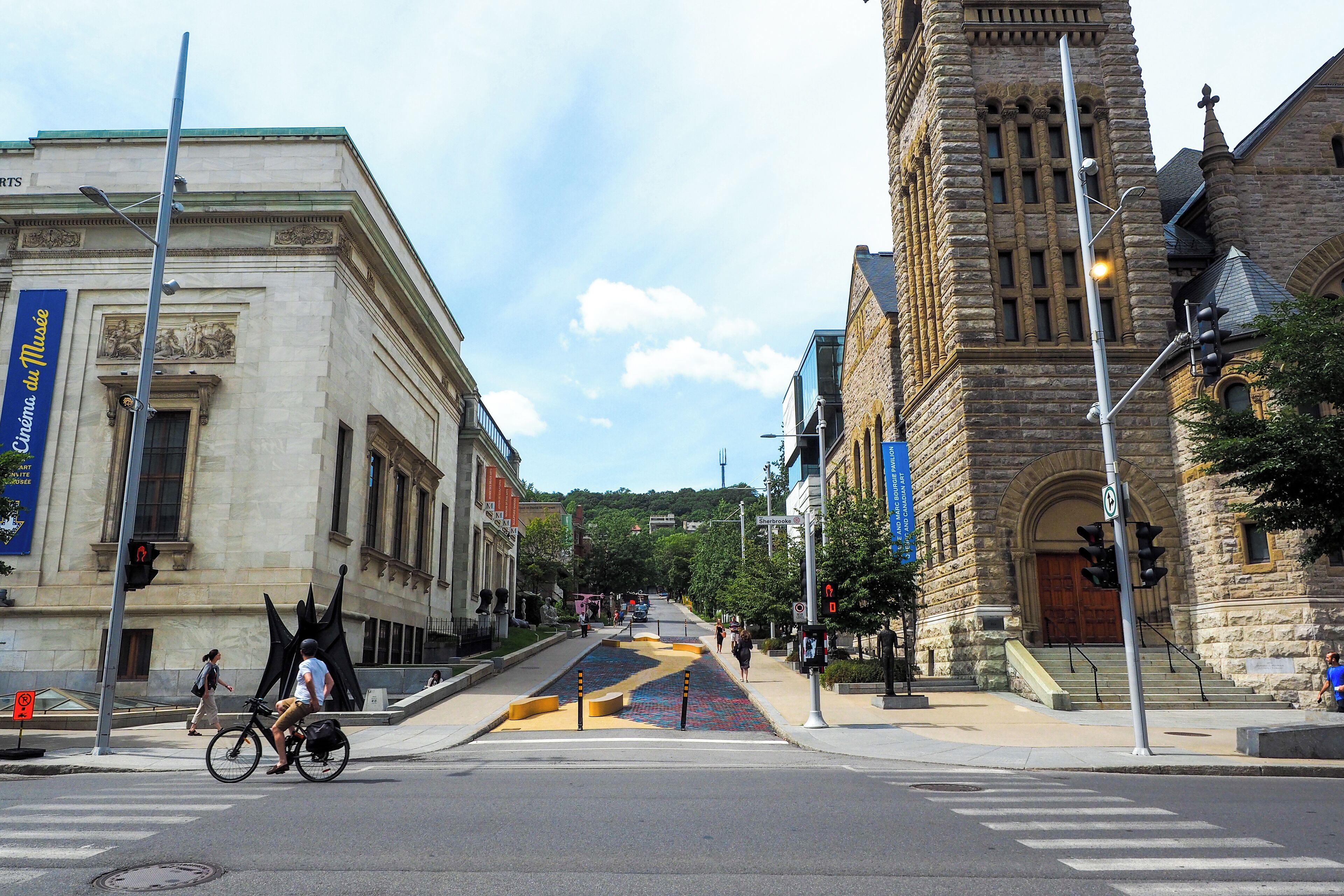 A street with a large stone building, a crosswalk, and a cyclist.